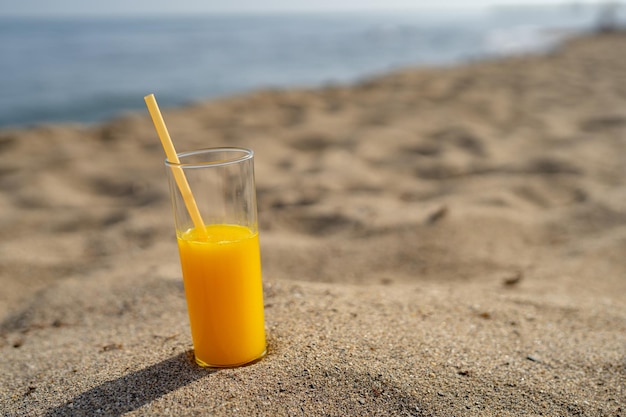 ein Glas Orangensaft mit einem Strohhalm steht auf dem Sand vor dem Hintergrund des Meeres