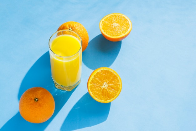 Ein Glas Orangensaft und Orangen auf blauem Grund. Konzept von Vitaminen, Tropen, Sommerzeit. Natürliches Licht. Flache Lage, Draufsicht.