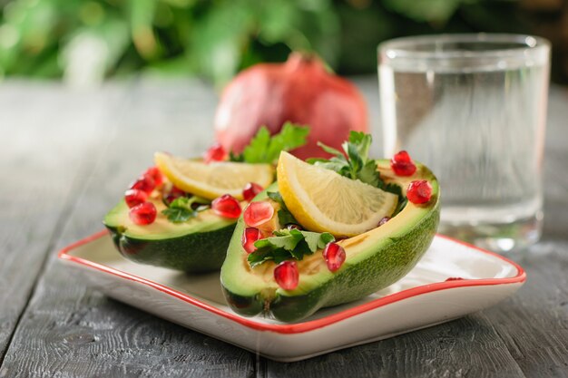 Ein Glas sauberes Wasser mit Avocadohälften, gefüllt mit Granatapfelkernen und Kräutern. Vegetarische Küche zur Gewichtsreduktion.