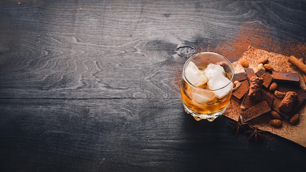 Ein Glas Schnaps. Whiskey. Schokoladensortiment. Holz auf der schwarzen Oberfläche. Ansicht von oben.