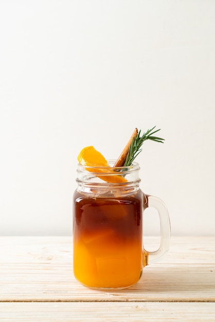 Ein Glas schwarzer Americano-Eiskaffee und eine Schicht Orangen- und Zitronensaft, dekoriert mit Rosmarin und Zimt auf einem Holztisch