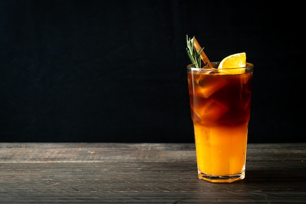 Foto ein glas schwarzer americano-eiskaffee und eine schicht orangen- und zitronensaft, dekoriert mit rosmarin und zimt