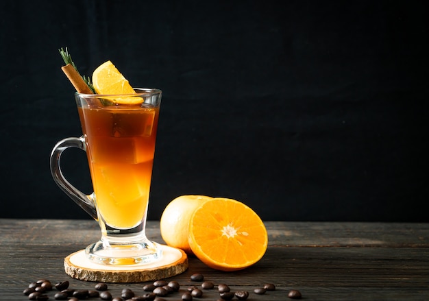 Ein Glas schwarzer Americano-Eiskaffee und eine Schicht Orangen- und Zitronensaft, dekoriert mit Rosmarin und Zimt