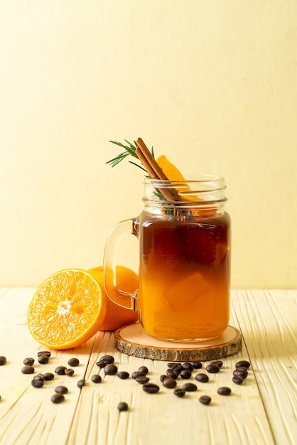 Ein Glas schwarzer Americano-Eiskaffee und eine Schicht Orangen- und Zitronensaft, dekoriert mit Rosmarin und Zimt