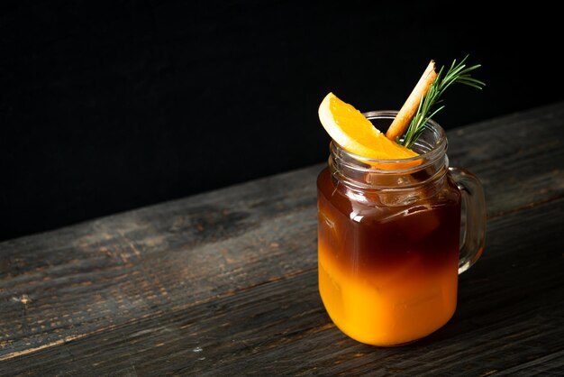 Ein Glas schwarzer Americano-Eiskaffee und eine Schicht Orangen- und Zitronensaft, dekoriert mit Rosmarin und Zimt