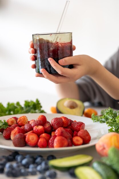 Ein Glas Smoothie aus Beeren in der Hand eines Kindes zu Hause in der Küche