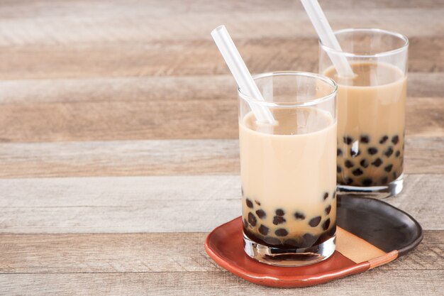 Ein Glas süßer Milchblasentee mit Tapiokaperlen und Stroh auf hölzernem Hintergrund. Speicherplatz kopieren