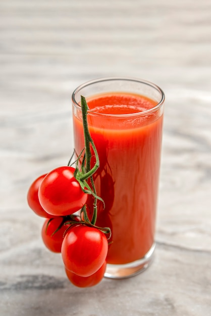 Ein Glas Tomatensaft und ein Zweig der kleinen Tomatenfahne. Kirschtomaten in einem roten Teller auf Marmorhintergrund. Platz zum Einfügen von Text oder Design