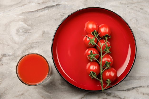 Ein Glas Tomatensaft und ein Zweig kleiner Tomatenbanner Kirschtomaten in einem roten Teller