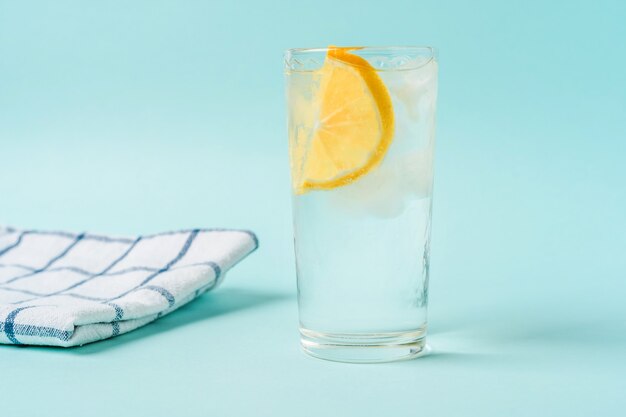 Ein Glas Wasser mit Eis und Zitrone auf hellblauem Hintergrund, das Konzept eines gesunden Lebensstils