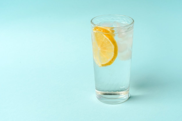 Ein Glas Wasser mit Eis und Zitrone auf hellblauem Hintergrund, das Konzept eines gesunden Lebensstils