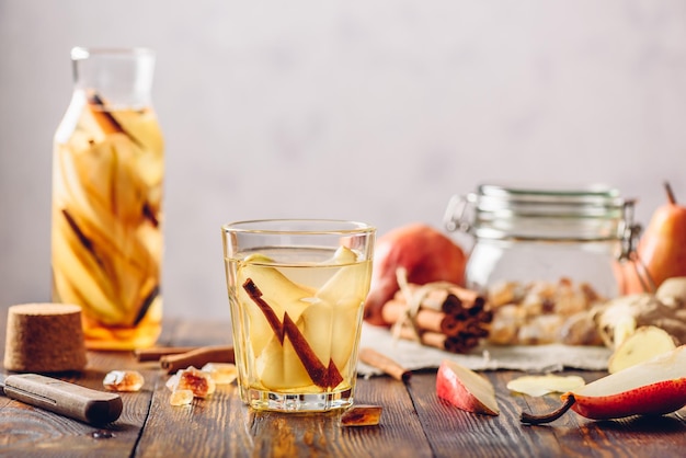 Ein Glas Wasser mit geschnittenen Birnen, Zimt, Ingwerwurzeln und einigen Zuckerzutaten