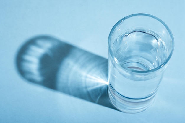 Ein Glas Wasser mit Schatten auf blauem Boden