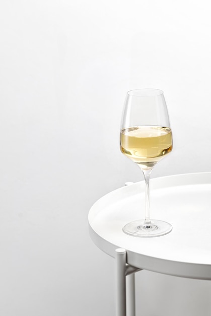 Ein Glas Weißwein auf einem weißen runden Tisch. Minimalismus. Elegant