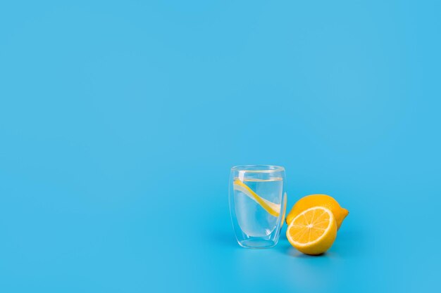 Ein Glasbecher mit einer Zitronenscheibe und einer halbierten Zitrone in der Nähe auf blauem Hintergrund Diät-Vitamin c