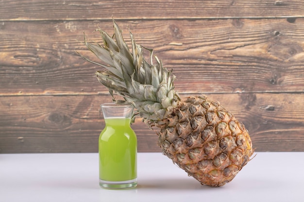 Ein Glaskrug grüner Saft mit einer gesunden Ananas auf einem Holztisch.