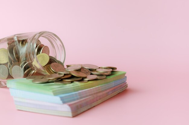 Ein Glaskrug mit Münzen und Banknoten auf rosa Hintergrund