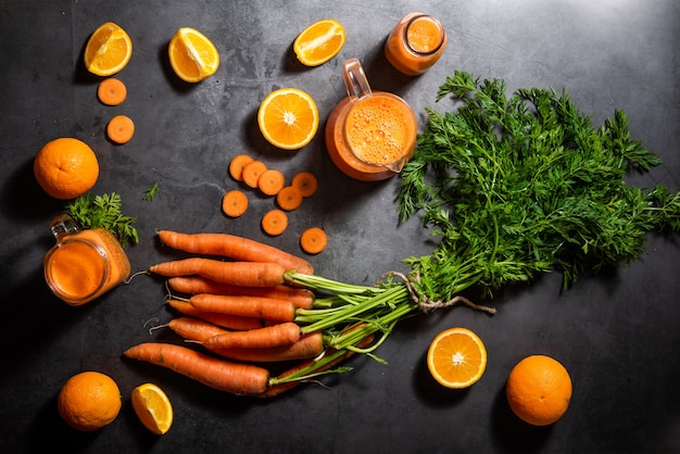 Ein Glaskrug und eine Flasche mit natürlichem Karotten- und Orangensaft und Karotten und mehreren Orangen