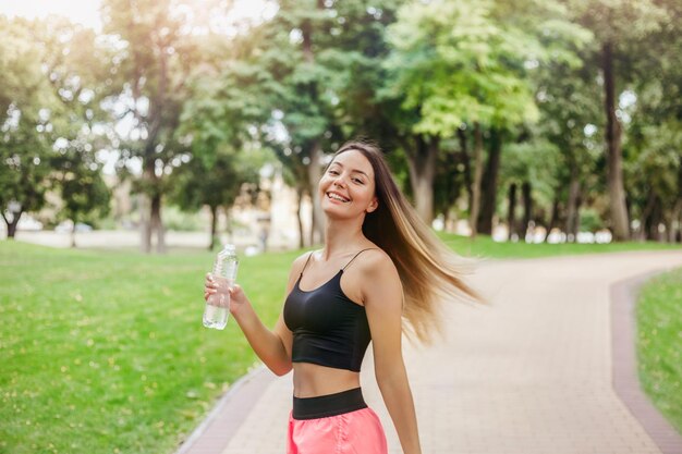 Ein glücklich lächelndes Mädchen ging mit einer Flasche Wasser im Park joggen, Sport treiben und einen gesunden Lebensstil führen