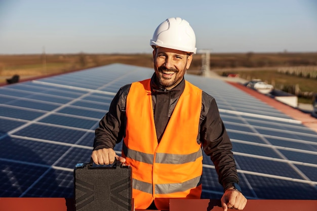 Ein glücklicher Arbeiter hat seine Arbeit mit Sonnenkollektoren erledigt und hält einen Werkzeugkasten in der Hand