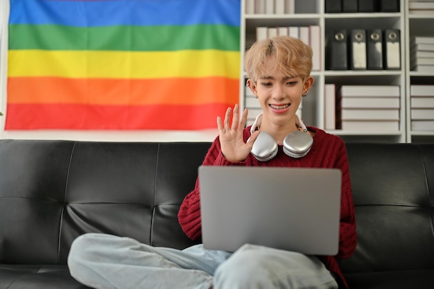 Ein glücklicher asiatischer schwuler Mann telefoniert über seinen Laptop mit seinen Freunden, während er zu Hause bleibt