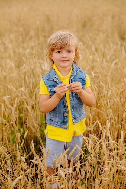 Foto ein glücklicher blonder junge in einer gelben jacke und einer jeansweste steht in einem weizenfeld