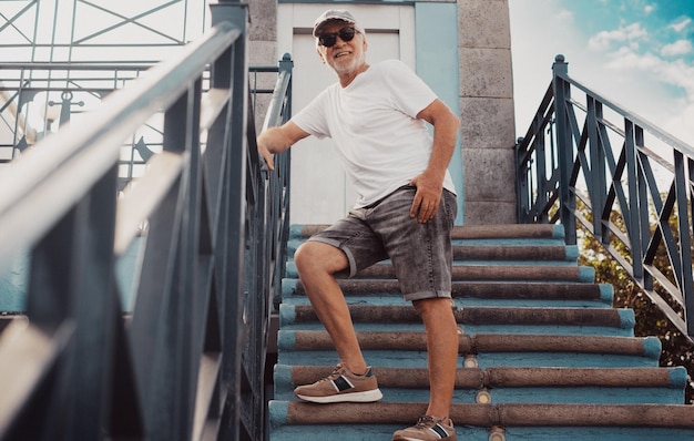 Foto ein glücklicher, hübscher älterer mann mit hut und sonnenbrille steht auf einer außentreppe