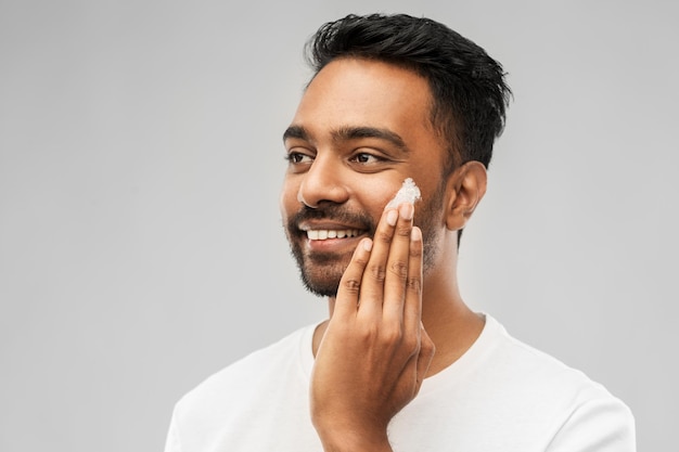 ein glücklicher indischer Mann, der Creme auf das Gesicht aufträgt