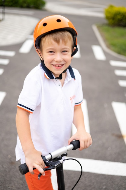 Ein glücklicher Junge auf einem Roller und mit einem Helm schaut in die Kamera und lächelt