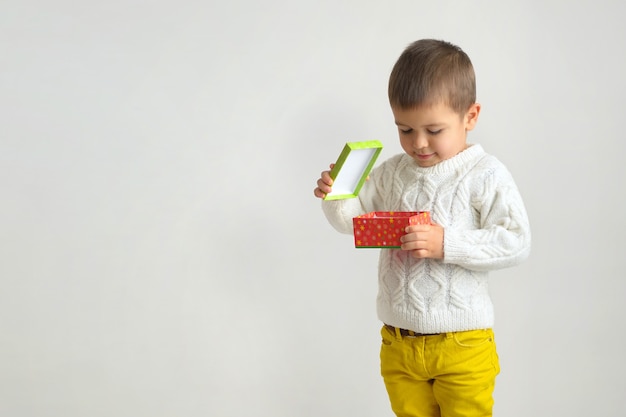 Ein glücklicher Junge in einem weißen Pullover und gelben Jeans, die Abdeckung der Geschenkbox halten