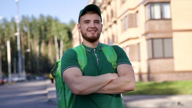 Foto ein glücklicher junger kurier in grüner uniform mit einer großen thermotürbe oder rucksack liefert essen von