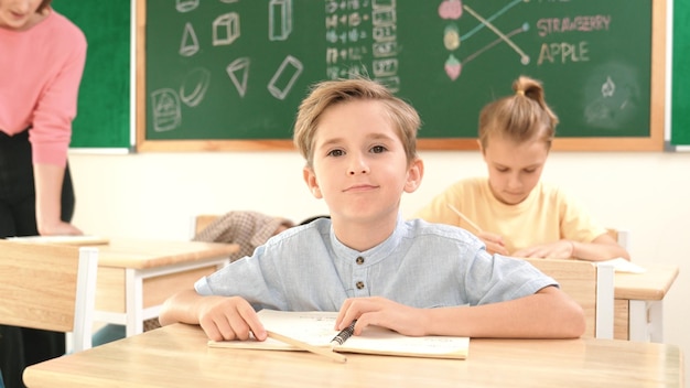 Ein glücklicher kaukasischer Junge schaut in die Kamera, während er Mathematik in der Pädagogik-Schule studiert.