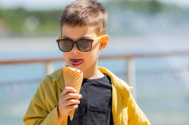 Ein glücklicher kleiner Junge isst im Sommer auf einem Spaziergang Eis in einem Waffelkegel