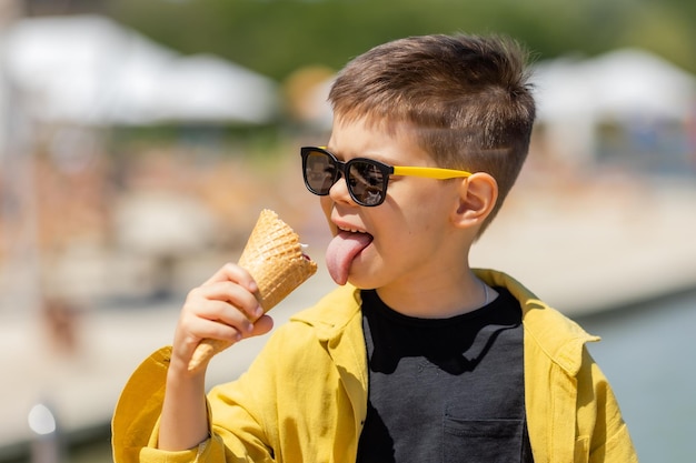 Ein glücklicher kleiner Junge isst im Sommer auf einem Spaziergang Eis in einem Waffelkegel