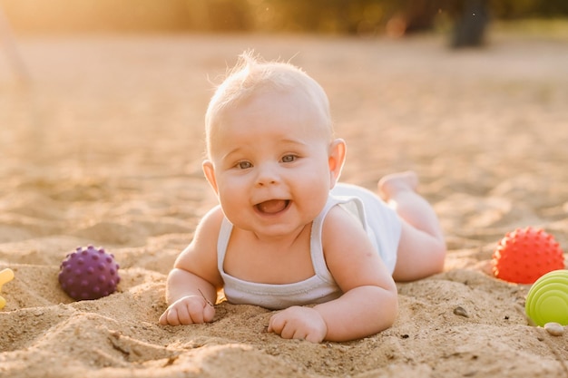 Ein glücklicher kleiner Junge liegt in den Strahlen der untergehenden Sonne an einem Sandstrand in der Nähe des Meeres