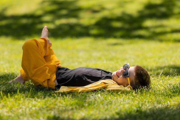 Ein glücklicher kleiner Junge mit Sonnenbrille liegt im Sommer auf dem Rasen