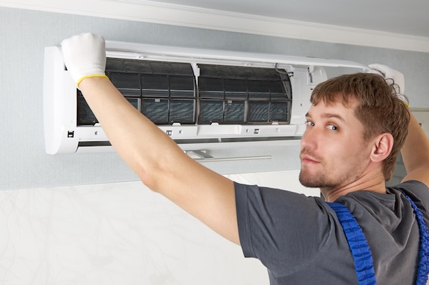 Ein glücklicher männlicher Techniker beginnt mit der Reparatur der Klimaanlage