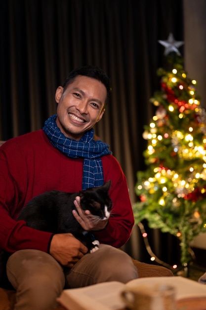Ein glücklicher Mann feiert seine Weihnachtsnacht mit seiner Katze zu Hause und sitzt zusammen auf einer Couch