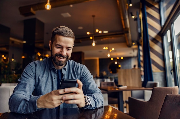 Ein glücklicher Mann sitzt im Café am Tisch und hängt an Social Media0