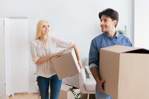 Ein glücklicher Mann und eine glückliche Frau, die Umzugsboxen tragen und eine neue Wohnung betreten