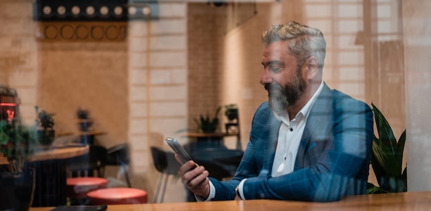 Ein glücklicher, reifer Geschäftsmann, der sein Telefon in einem Café-Restaurant benutzt