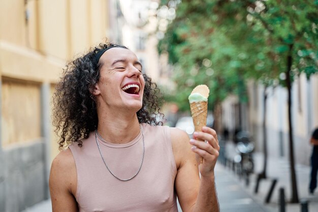 ein glücklicher schwuler Mann geht die Straße entlang mit einem Eiscreme-Kegel in der Hand und lacht laut