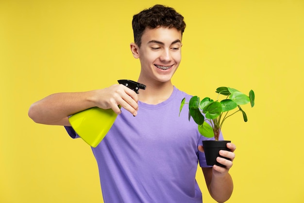 Ein glücklicher Teenager mit Klammern hält einen Blumentopf und sprüht ihn isoliert auf gelben Hintergrund