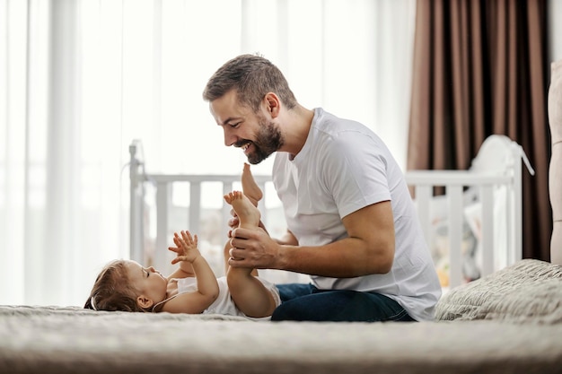 Ein glücklicher Vater macht Babyübungen mit seinem Baby in einem Schlafzimmer