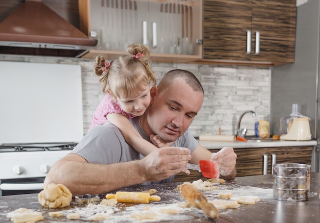 Ein glücklicher Vater und seine kleine Tochter kochen zusammen Kekse in der Küche. gemeinsames Kochen, Familienwerte