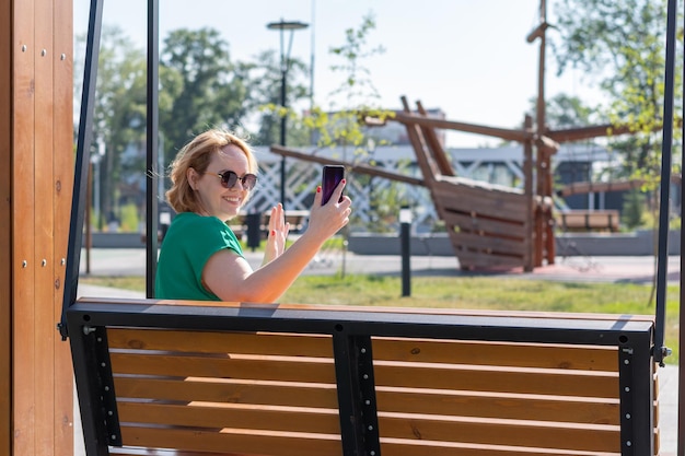Ein glückliches, attraktives Studentenmädchen mit Sonnenbrille, das ein Selfie-Foto am Telefon macht und mit Freunden auf der Straße chattet