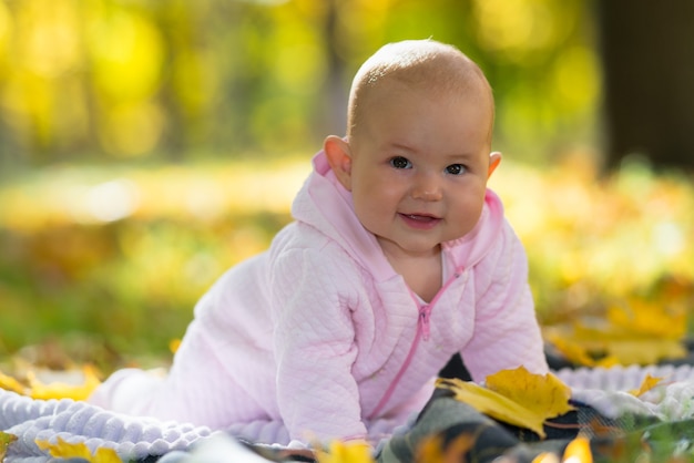 Ein glückliches Baby, das lernt, auf einem Picknick-Teppich zwischen Herbstblättern in einer hellen Herbstpark-Szene zu kriechen.