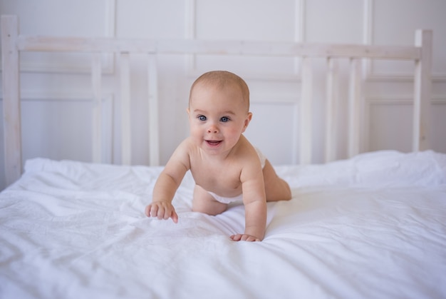 Ein glückliches Baby in einer Windel krabbelt auf einer weißen Baumwolldecke auf dem Bett im Zimmer