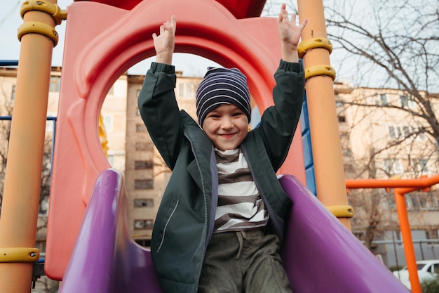 ein glückliches Baby-Kind-Junge fährt im Herbst auf einer Rutsche auf dem Spielplatz