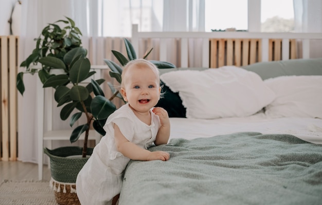 Ein glückliches Baby steht neben dem Bett im Schlafzimmer